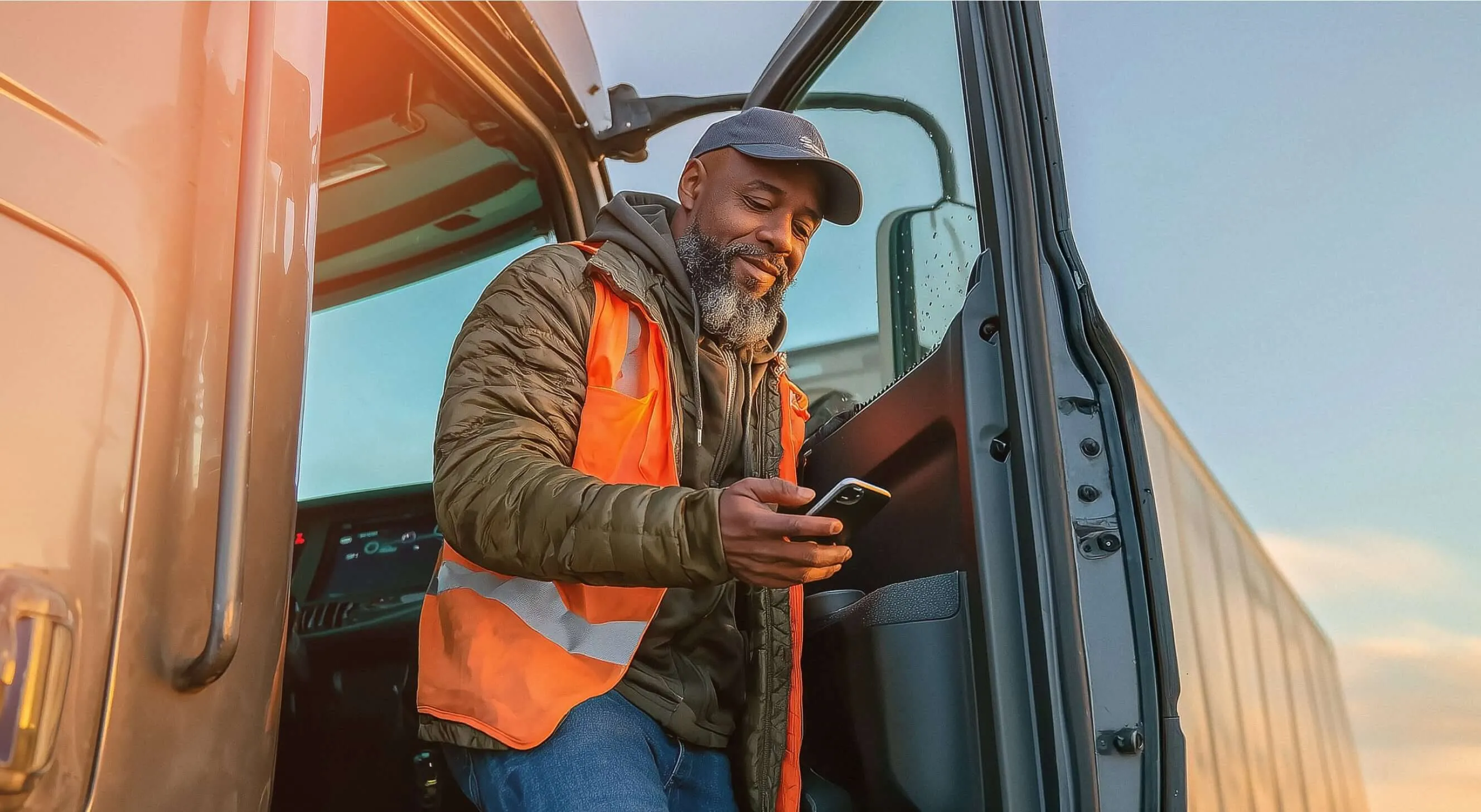 A male delivery truck driver looking at his mobile phone while exiting his semi-trailer truck