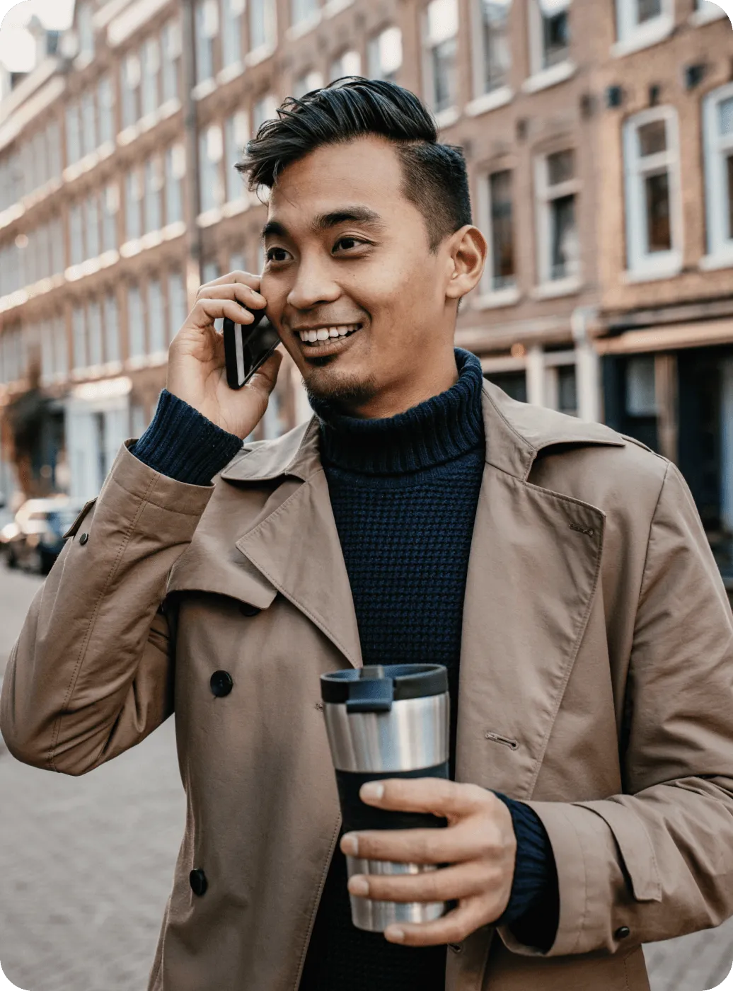 A man taking a phone call outside while holding a tumbler