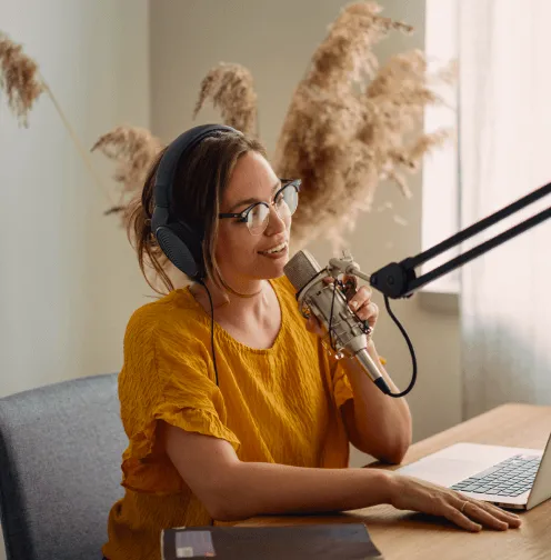 A woman on headphones hosting a virtual event at home using a big mic in front of her laptop
