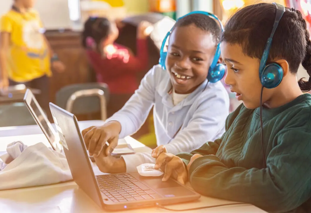 Two young kids smile as they look at a laptop screen